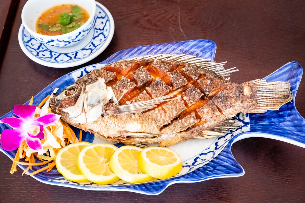 Whole fried fish on a Thai blue ceramic platter with fresh herbs